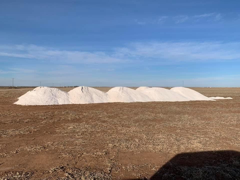 Pale ag lime piles lined up on a hillside field