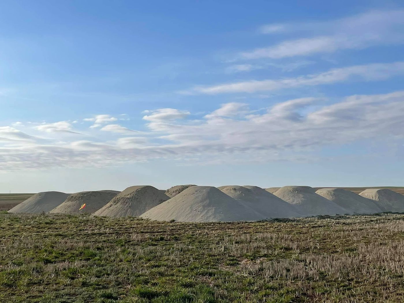 Row of pale ag lime piles on open prairie under a blue sky