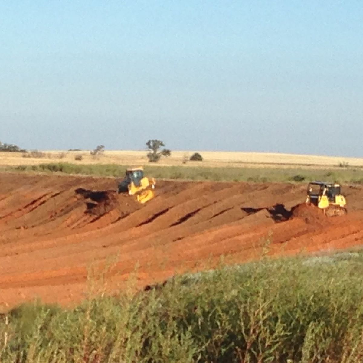 Two yellow dozers working a cut of red dirt on open Kansas or Oklahoma prairie