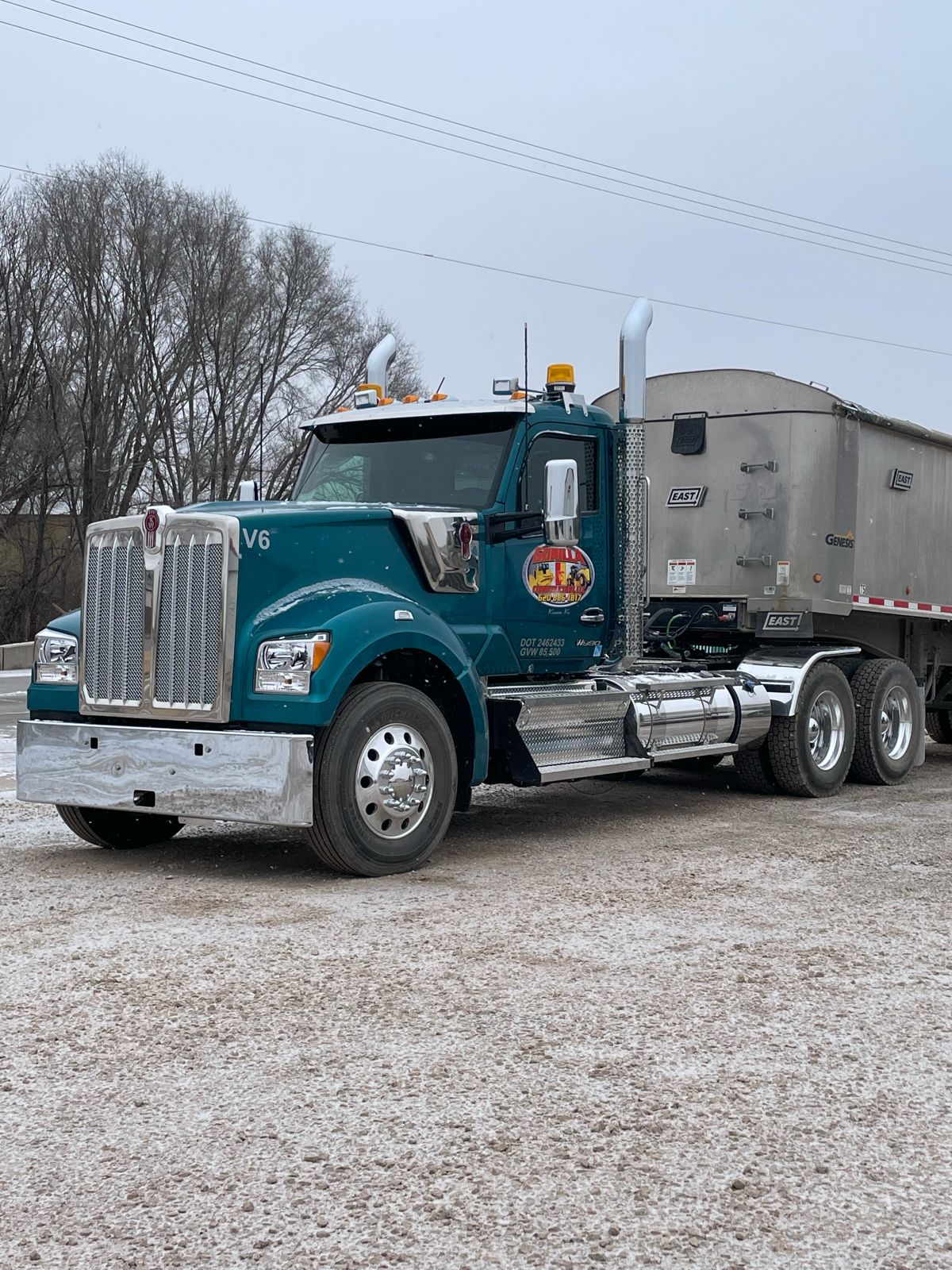 Teal Kenworth semi with an aluminum end dump trailer parked on a gravel lot in light snow